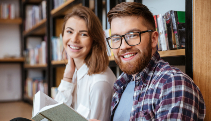 Male and female students reading a book in the library