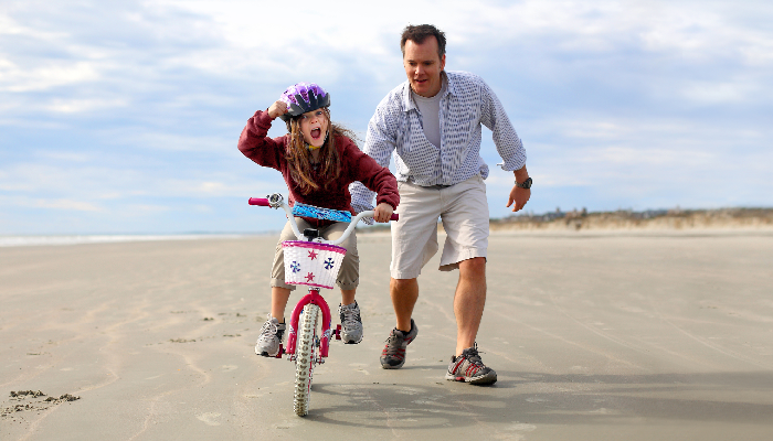 father helping daughter to ride a bike