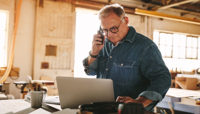 man in workshop on laptop and phone