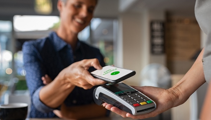 Woman in coffee shop tapping her phone as payment