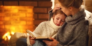 mother and daughter reading book by the fire