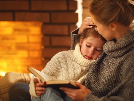 mother and daughter reading book by the fire