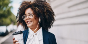 business woman with headphones in walking with coffee in hand