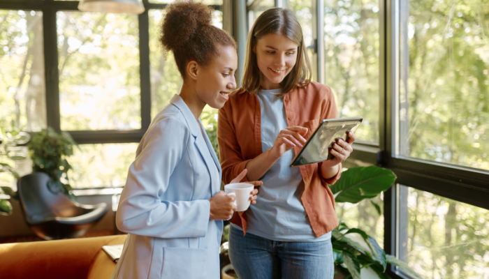 two young woman having coffee on tablet in office