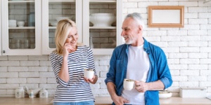 Mature woman and man spending time together standing at home kitchen drink tea