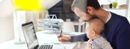 father at home office working with child on his lap