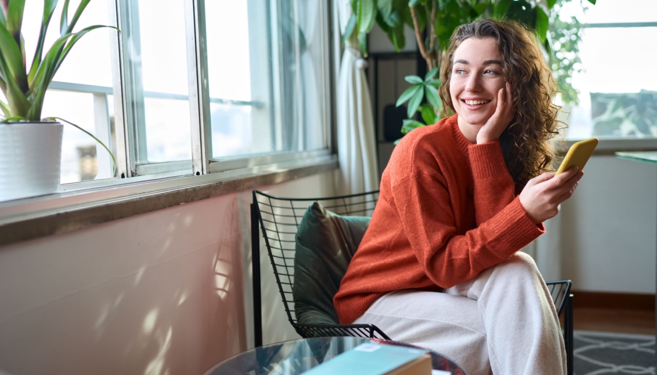 Happy young woman sitting on chair holding mobile phone