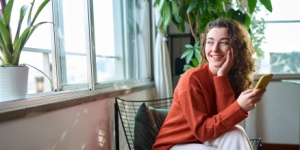 Happy young woman sitting on chair holding mobile phone