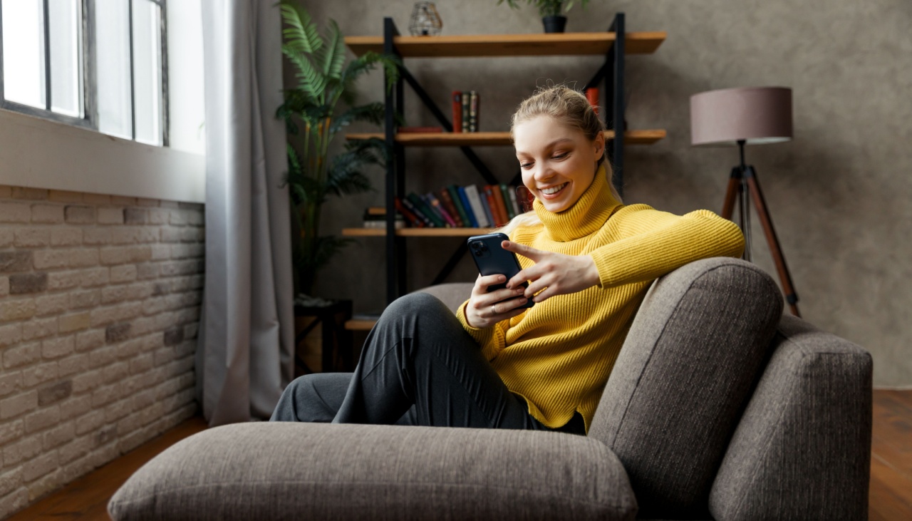 Cheerful young woman using mobile phone while sitting on a sofa at home