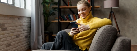 Cheerful young woman using mobile phone while sitting on a sofa at home