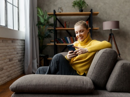 Cheerful young woman using mobile phone while sitting on a sofa at home