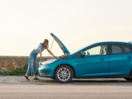 young woman looking under the hood of her broken car