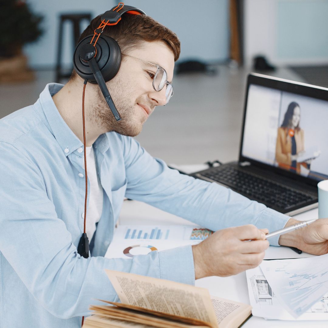Young business man in front of laptop with headset on his head while looking at business documents on his desk